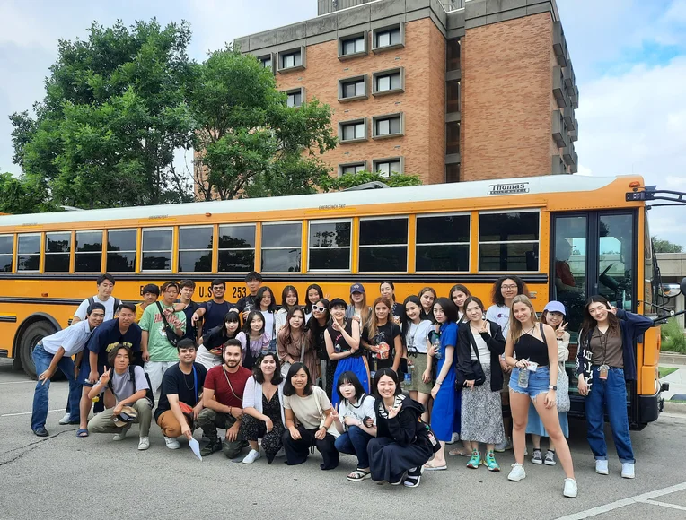 Summer Institute students pose for photo in front of a yellow school bus before heading out on a field trip