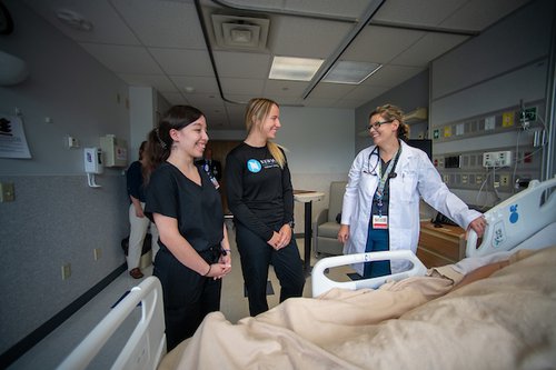 Two students and one doctor looking at a hospital bed