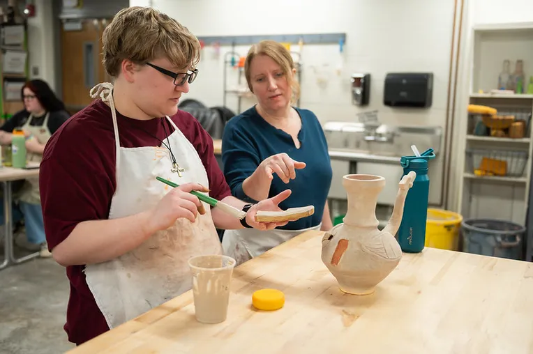 Student painting with teachers guidance