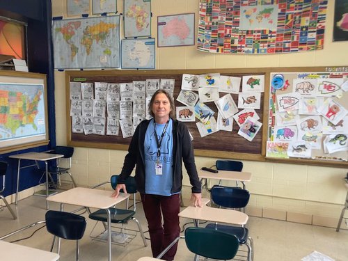 A teacher, Peter Cybula, stands in front of a bulletin board in his classroom.