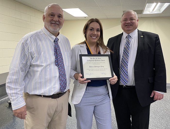 A woman holds a framed award certificate with two men in suitcoats on either side of her.