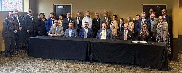 Group of men and women both seated at and standing behind an eight-feet-long table draped with a black cloth.