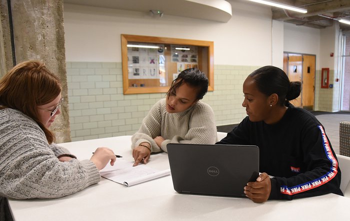 Three students with notebook and laptop sitting at a table