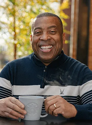 Man smiles while holding a coffee mug.